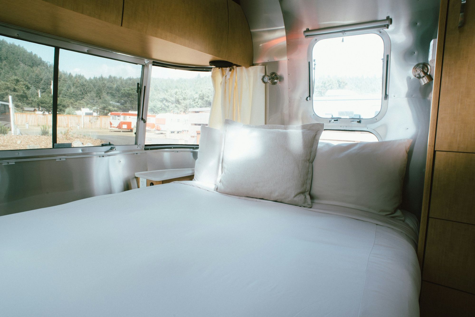 A bed with white sheets in the back of a travel trailer