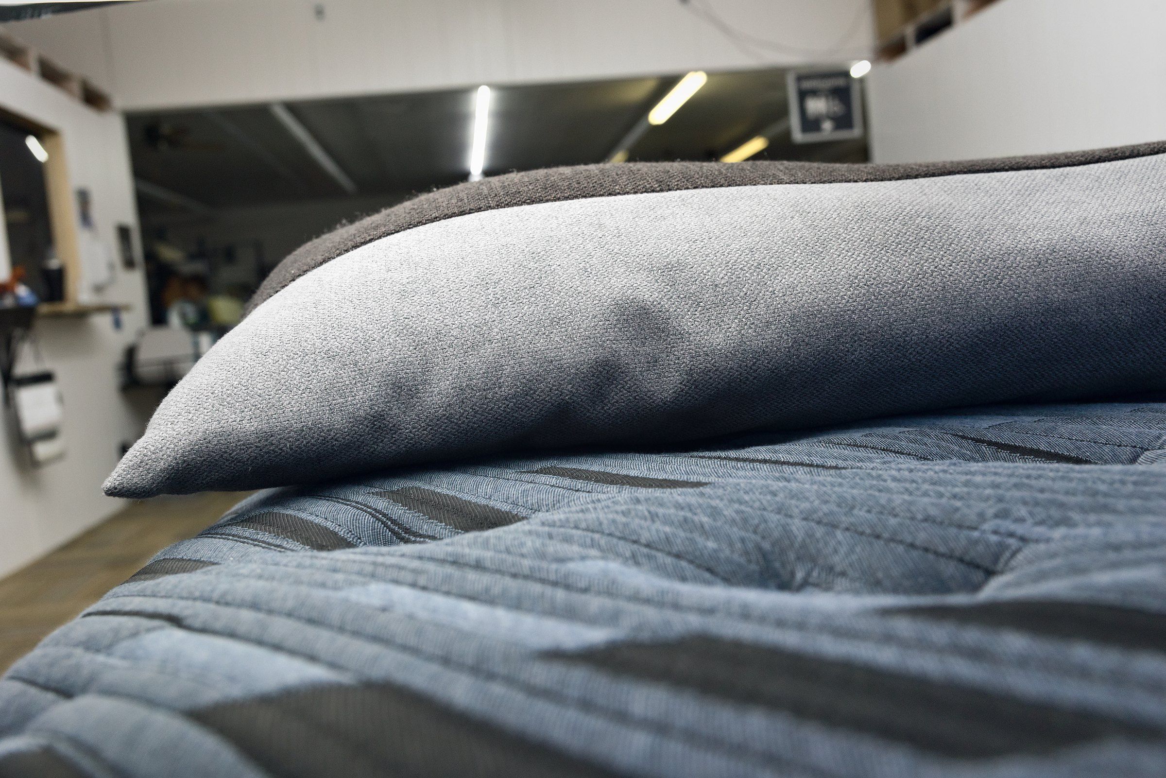 A grey pillow resting on the quilted top of a mattress